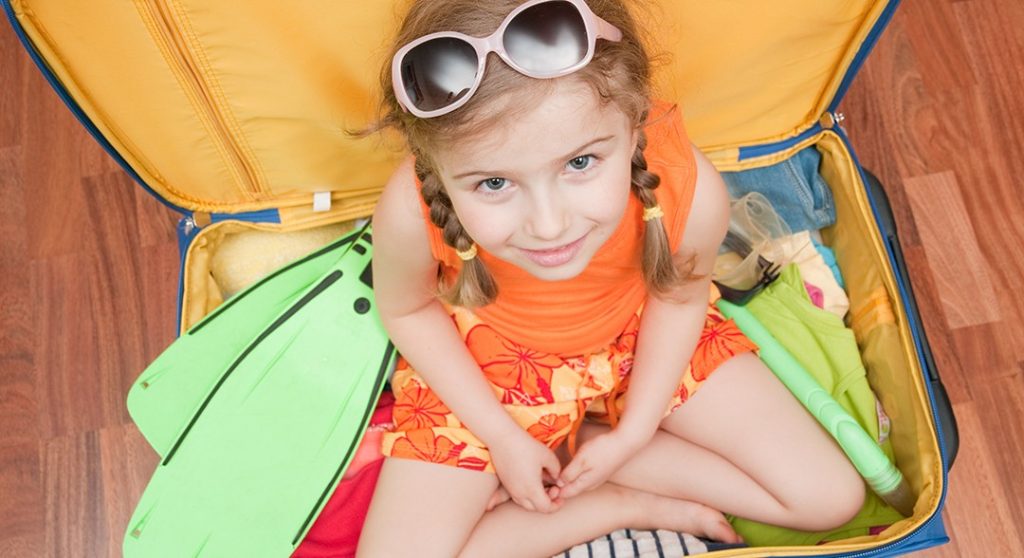 Child with swimming things sitting in suit case